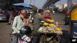FILE - Jitendra Prasad takes money for bananas sold to an autorickshaw driver near Azadpur Mandi, Asia's largest wholesale market for fruits and vegetables in New Delhi, India, Nov. 22, 2016. India has slightly trimmed its economic outlook for 2016.