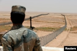 FILE - A member of the Saudi border guards force stands guard next to a fence on Saudi Arabia's northern borderline with Iraq, July 14, 2014.