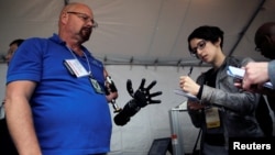 A journalist takes notes while talking with Johnny Matheny (L), from the Johns Hopkins University Applied Physics Lab, as he shows his prosthetic hand during the DARPA (Defense Advanced Research Projects Agency) Demo Day exhibition at the Pentagon in Wash