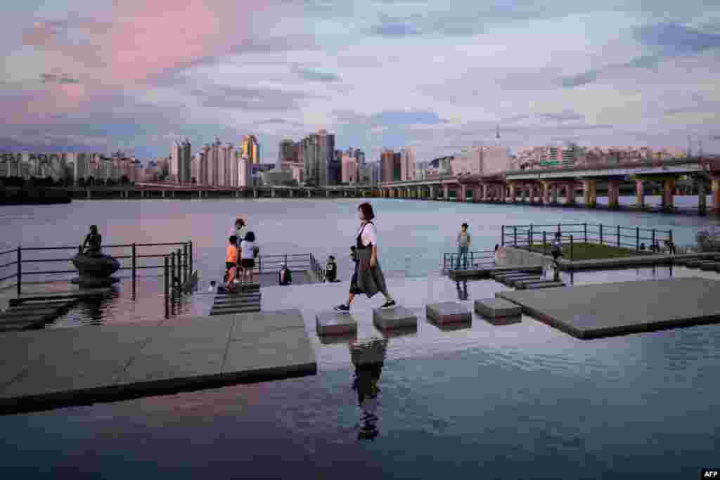 A woman walks over stepping-stones before the Han river and Seoul&#39;s skyline at Yeouido park, South Korea.