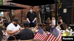 As Phase One of reopening begins in Northern Virginia, a waiter in a face mask to protect against the coronavirus (COVID-19) serves diners seated outdoors at a restaurant in Alexandria, Virginia, U.S., May 29, 2020. 