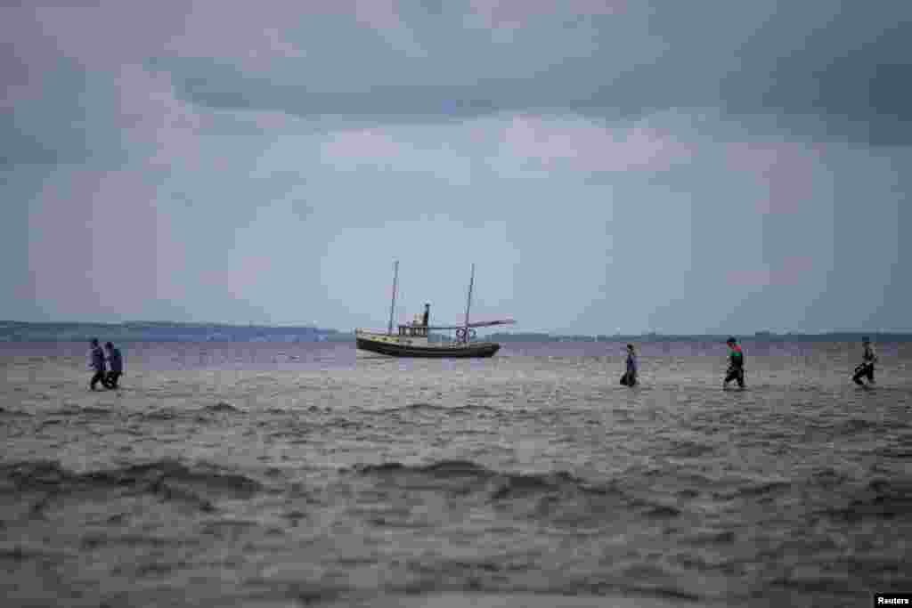 People walk through Puck Bay during the Herring March with a yacht in the background, in Kuznica, Poland, Aug. 19, 2017.