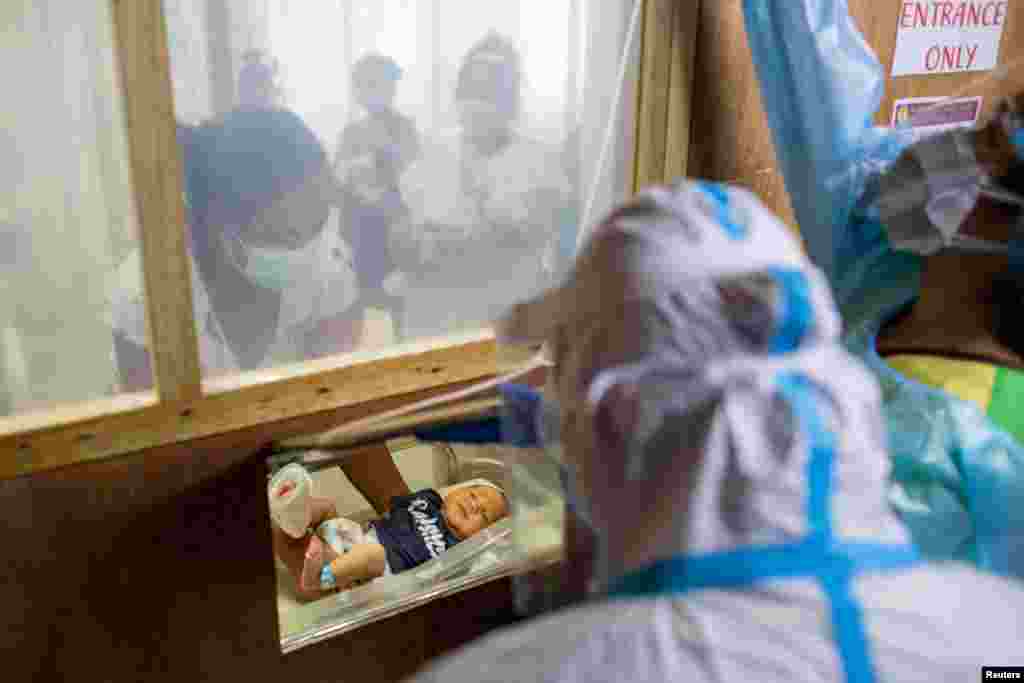 A mother carries her newborn baby towards a makeshift window for health workers to tend to, at the COVID-19 isolation area of the government-run Dr. Jose Fabella Memorial Hospital, amid the coronavirus outbreak, in Manila, Philippines.