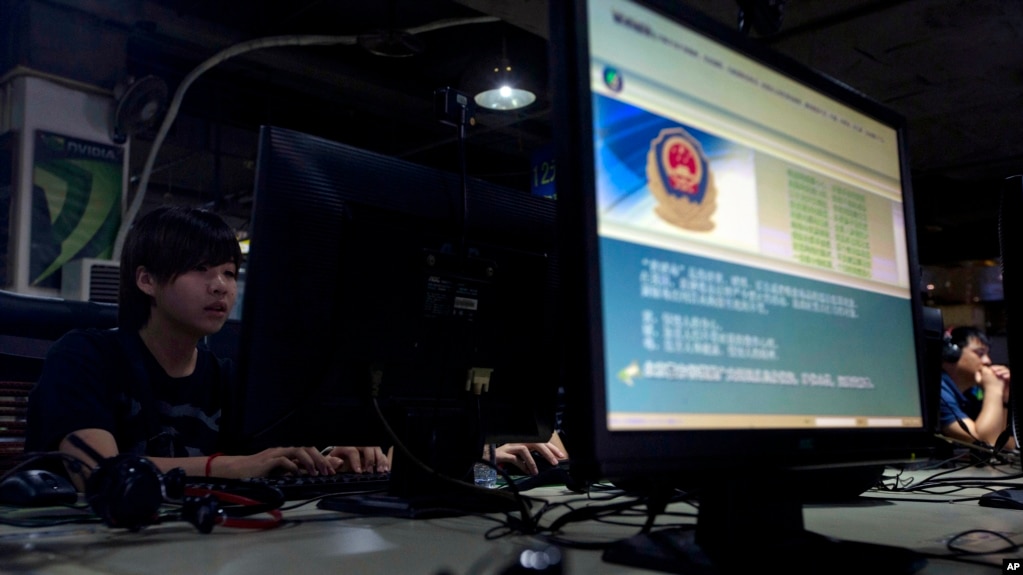 FILE - Computer users sit near a monitor display with a message from the Chinese police on the proper use of the Internet at an Internet cafe in Beijing, China.