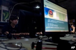 FILE - Computer users sit near a monitor display with a message from the Chinese police on the proper use of the Internet at an Internet cafe in Beijing, China.