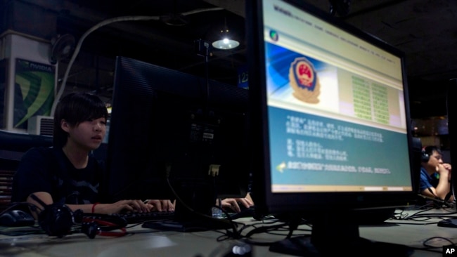 FILE - Computer users sit near a monitor display with a message from the Chinese police on the proper use of the Internet at an Internet cafe in Beijing, China, in this this Aug. 19, 2013 file photo.
