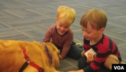 Two boys waiting to catch a flight at Dulles International Airport get to know a People Animals Love therapy dog. (D. Block/VOA)