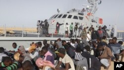 Rescued migrants are seated next to a coast guard boat in the city of Khoms, around 120 kilometers (75 miles) east of Tripoli, Libya, Tuesday, Oct. 1, 2019. (AP Photo/Hazem Ahmed)