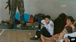 FILE - In an undated image taken from television early during the siege, hostages sit on a floor in a gym as a hostage-taker stands with his left foot on a book, apparently with a device connected to a chain of explosives, in the school in Beslan, Russia. The siege began Sept. 1, 2004.