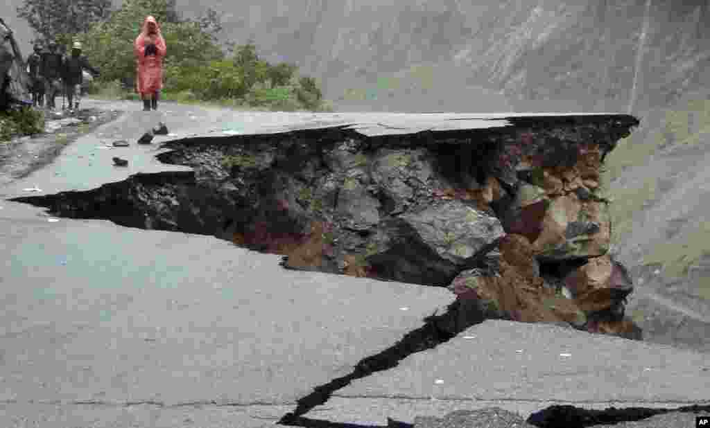 Indian people walk on a road which was caved in after incessant rains on Rishikesh-Mana highway near Joshimath district in northern Indian state of Uttarakhand, India, June 17, 2013.