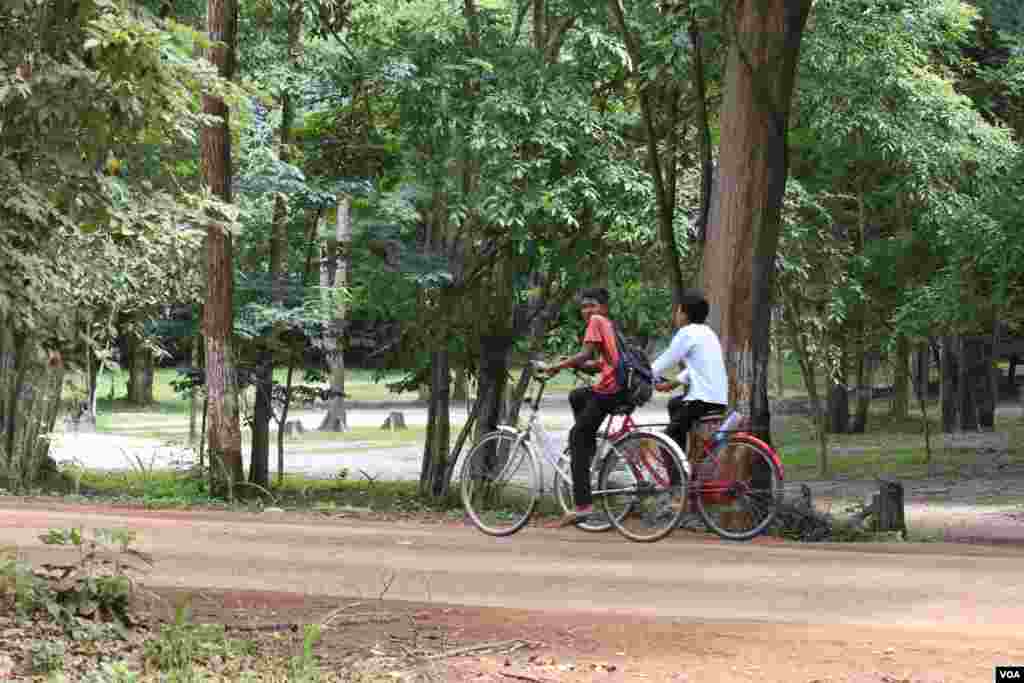 កុមារាពីរនាក់ជិះកង់លើផ្លូវលំមួយនៅក្នុងបរិវេណតំបន់ប្រាសាទសំបូរព្រៃគុក កាលពីថ្ងៃទី១៣ ខែកក្កដា ឆ្នាំ២០១៧។ (ស៊ុន ណារិន/VOA)