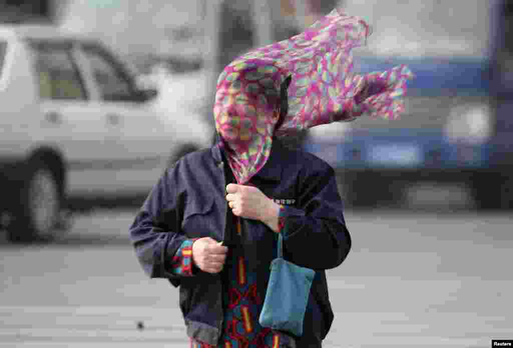 A strong wind blows a scraf in a woman&#39;s face as she crosses a street in Shenyang, Liaoning province, China.