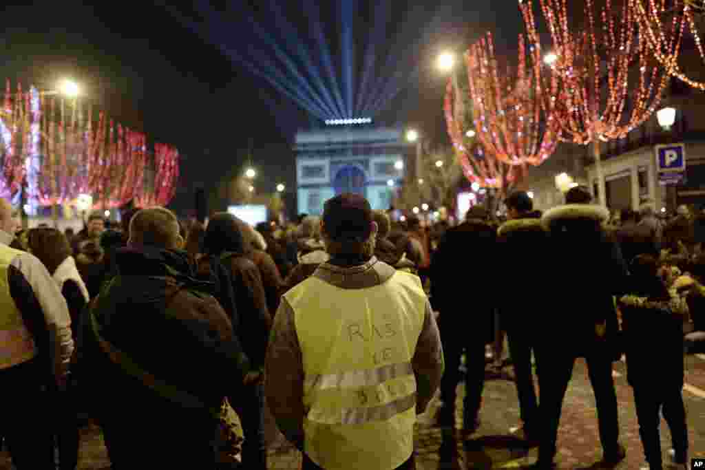 Un manifestante de chaleco amarillo mira las iluminaciones sobre el Arco de Triunfo antes de las celebraciones del Día de Año Nuevo en los Campos Elíseos, en París.