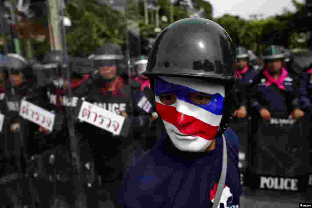 An anti-government protester wearing a mask painted in the colors of the Thai national flag looks on as riot police officers stand guard outside the parliament in Bangkok. Thailand&#39;s parliament was due to debate a political amnesty bill as anti-government protesters marched to try to get it scrapped, saying it could let ex-premier Thaksin Shinawatra return from exile without having to serve a jail sentence.