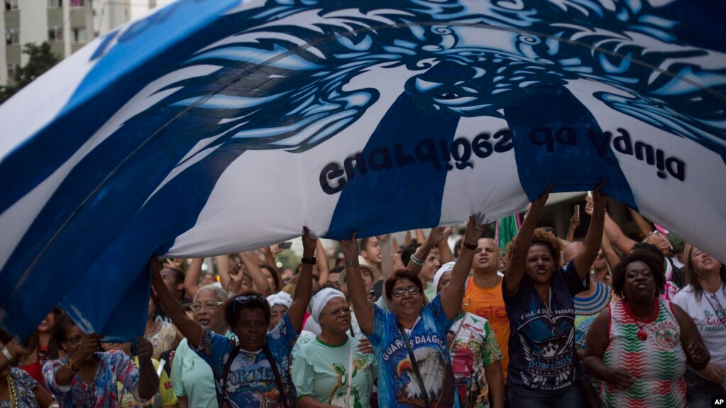 Samba school members wave a giant flag as they march toward the Sambadrome during a protest against mayor Marcelo Crivella in Rio de Janeiro, Brazil, Saturday, June 17, 2017. The samba schools are protesting the decision by Crivella to cut carnival funding in half for the 2018 Carnival parade. (AP Photo/Leo Correa)