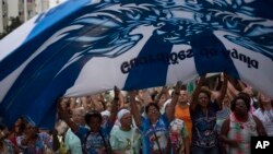 Samba school members wave a giant flag as they march toward the Sambadrome during a protest against mayor Marcelo Crivella in Rio de Janeiro, Brazil, Saturday, June 17, 2017. The samba schools are protesting the decision by Crivella to cut carnival funding in half for the 2018 Carnival parade. (AP Photo/Leo Correa)