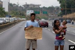 FILE - A demonstrator holds up a poster that reads in Spanish "Four weeks without water" during a protest demanding the service suspended one month ago, in Caracas, Venezuela, April 27, 2018.