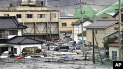 An earthquake-triggered tsunami washes away a warehouse and vehicles in Kesennuma, Miyagi prefecture (state), Mar 11 2011