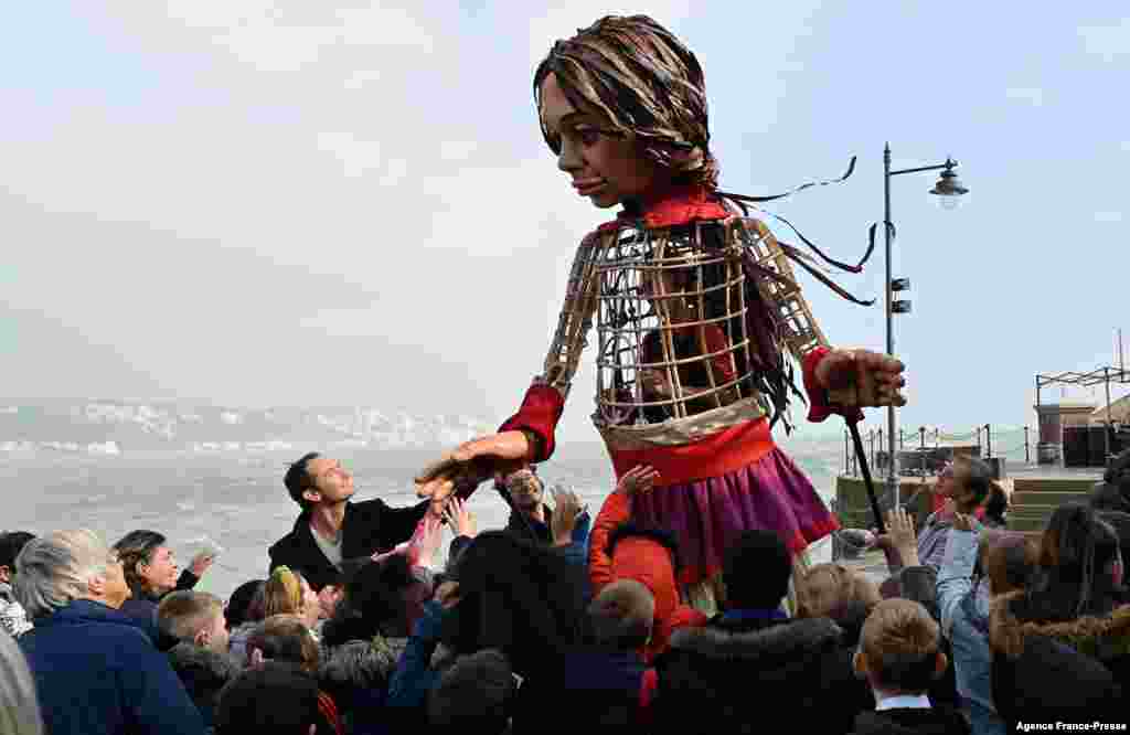 British actor Jude Law holds the hand of &#39;Little Amal&#39;, a puppet depicting a Syrian refugee girl, as she walks along the sea front at the harbor in Folkestone, southeast England, after arriving from Calais, as part of the international art project The Walk.