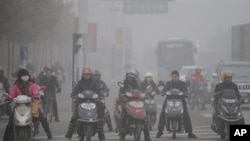 Chinese motorists ride their electric bikes in heavy fog down a street in Hefei, east China's Anhui province, 25 Nov 2009