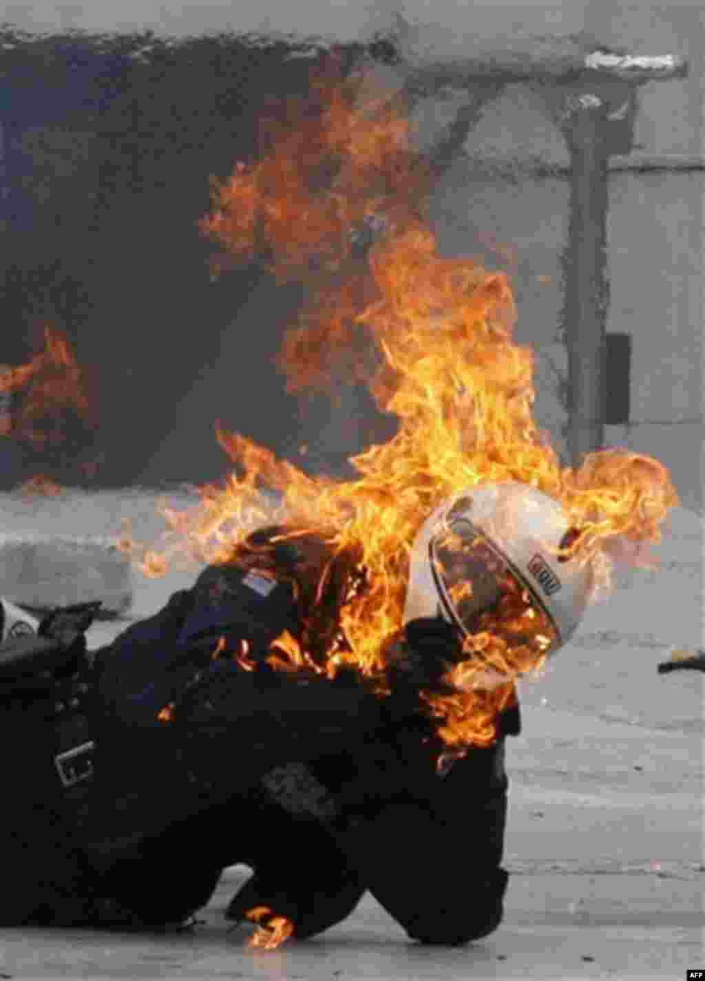 A motorcycle policeman tries to remove his helmet as he burns after protesters throw a petrol bomb in Athens, Wednesday, Fe. 23, 2011. Scores of youths hurled rocks and petrol bombs at riot police after clashes broke out Wednesday during a mass rally taki