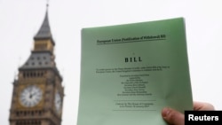 A journalist poses with a copy of the Brexit Article 50 bill, introduced by the government to seek parliamentary approval to start the process of leaving the European Union, in front of the Houses of Parliament in London, Jan. 26, 2017.