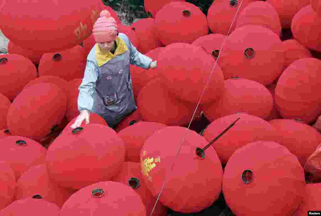 Seorang pekerja berjalan di antara lentera-lentera yang baru dibuat untuk persiapan Festival Musim Semi di Wenxian, provinsi Henan, China.