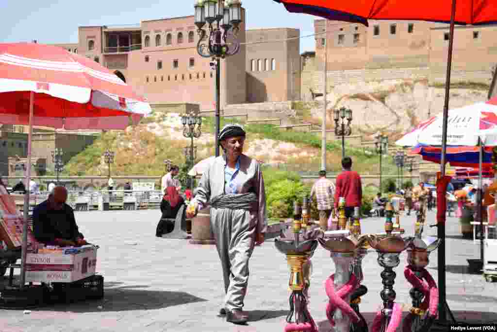 Erbil Kalesi&rsquo;nin eteğindeki meydanda günlük hayat, sokak satıcıları, minik çay ocakları ve ilk baharda bile rahatsız etmeye başlayan sıcaktan korunmaya çalışanların sığındığı şemsiyeler&hellip;