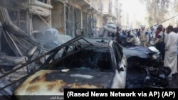 ພວກຄົນຈຳນວນໜຶ່ງເຕົ້າໂຮມກັນຢູ່ອ້ອມຮອບ ຊາກຫັກພັງຂອງຕຶກ ແລະພວກລົດ ທີ່ໄດ້ຖືກທຳລາຍ ຫຼັງຈາກການໂຈມຕີທາງອາກາດ ໃນເມືອງ Al-Bab ນອກຊານເມືອງ Aleppo ຂອງຊີເຣຍ, ວັນທີ 5 ຕຸລາ 2015, ພາບນີ້ເປີດເຜີຍໂດຍ Rased News Network.