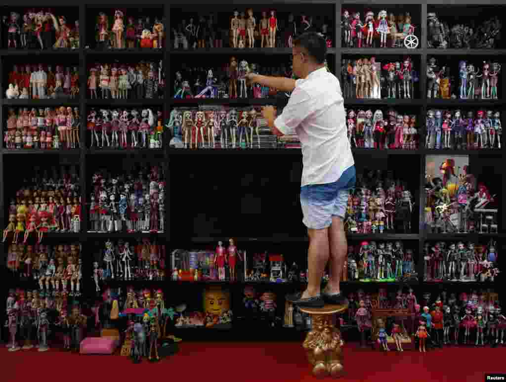 Barbie doll collector Jian Yang stands on a stool as he arranges part of his collection at his home in Singapore. The 33-year-old Singaporean favours minimalist decor with 6,000 Barbies and 3,000 dolls of other kinds dominate three sides.