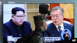 A South Korean marine passes by a TV screen showing file footage of South Korean President Moon Jae-in and North Korean leader Kim Jong Un, left, during a news program at the Seoul Railway Station in Seoul, South Korea, April 18, 2018.