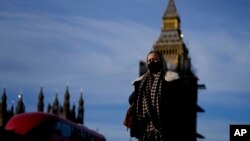 FILE - A woman wearing a mask crosses Westminster Bridge in London, Dec. 9, 2021. British Prime Minister Boris Johnson has hastened the availability of COVID-19 booster shots to stem the spread of the coronovirus omicron variant. 