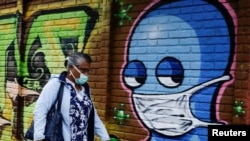 A woman wearing a protective face mask walks by a wall with graffitis after health authorities reverse the measures of reopening following the increase in cases of the coronavirus disease (COVID-19) in San Jose, Costa Rica July 13, 2020. 
