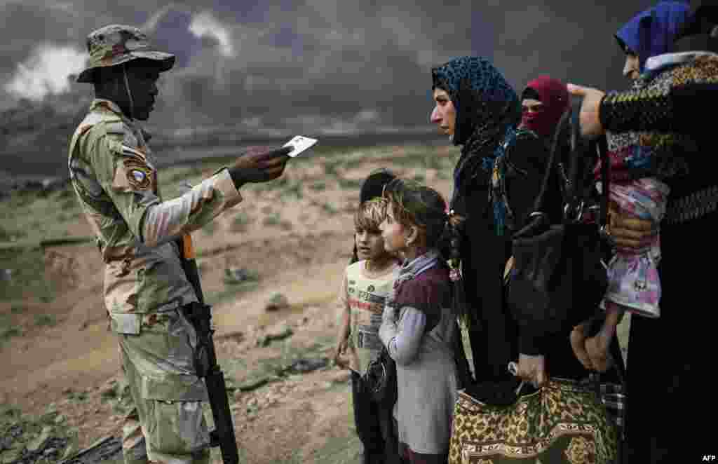 A member of the Iraqi forces trying to retake the city of Mosul talks to families fleeing the ongoing operation against the Islamic State, in an area near Qayyarah.