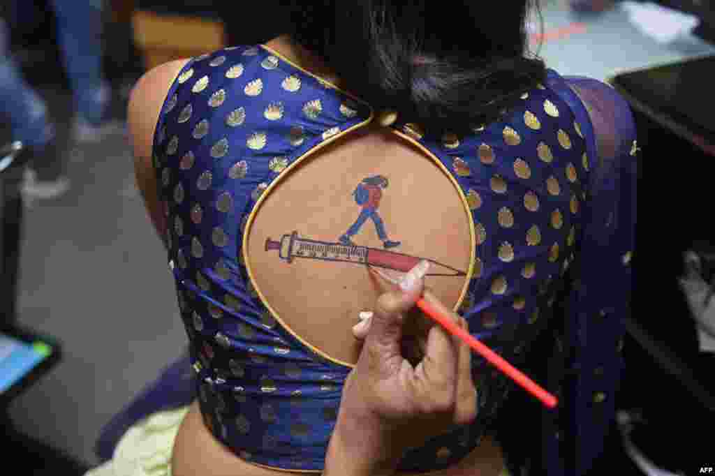 A Garba (folk dance) participant gets her back painted with an awareness message on vaccination against COVID-19 during the ongoing Navratri festival in Ahmedabad, India.