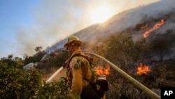 A firefighter douses the grass with water along a hillside on a wildfire in Azusa, Calif., Monday, June 20, 2016. (AP Photo/Ringo H.W. Chiu)