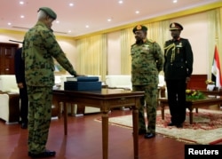 FILE L- Defence Minister Awad Mohamed Ahmed Ibn Auf (L), an ex-military intelligence chief is sworn in as first vice president in front of Sudan's President Omar al-Bashir during a swearing in ceremony of new officials after Bashir dissolved the central and state governments in Khartoum, Feb. 24, 2019.