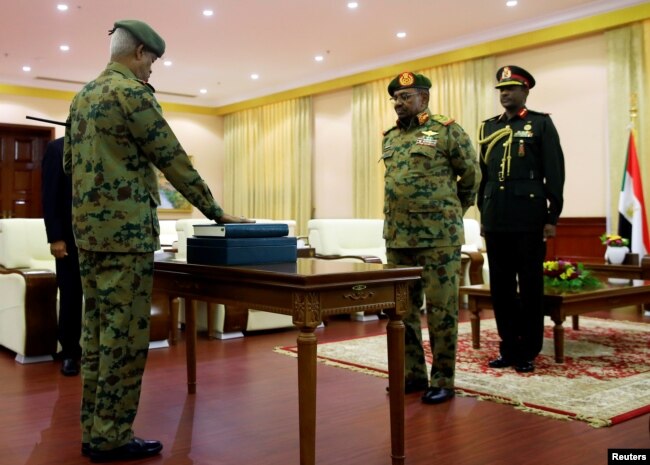 FILE - DefenSe Minister Awad Mohamed Ahmed Ibn Auf (L), an ex-military intelligence chief is sworn in as first vice president in front of former President Omar al-Bashir during a swearing in ceremony of new officials after Bashir dissolved the central and state governments in Khartoum, Sudan, Feb. 24, 2019