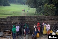 Golfers walk in the background as Kenyans watch bulldozers demolish dozens of houses to make way for a new road in the Kibera slum in Nairobi, Kenya, July 23, 2018.