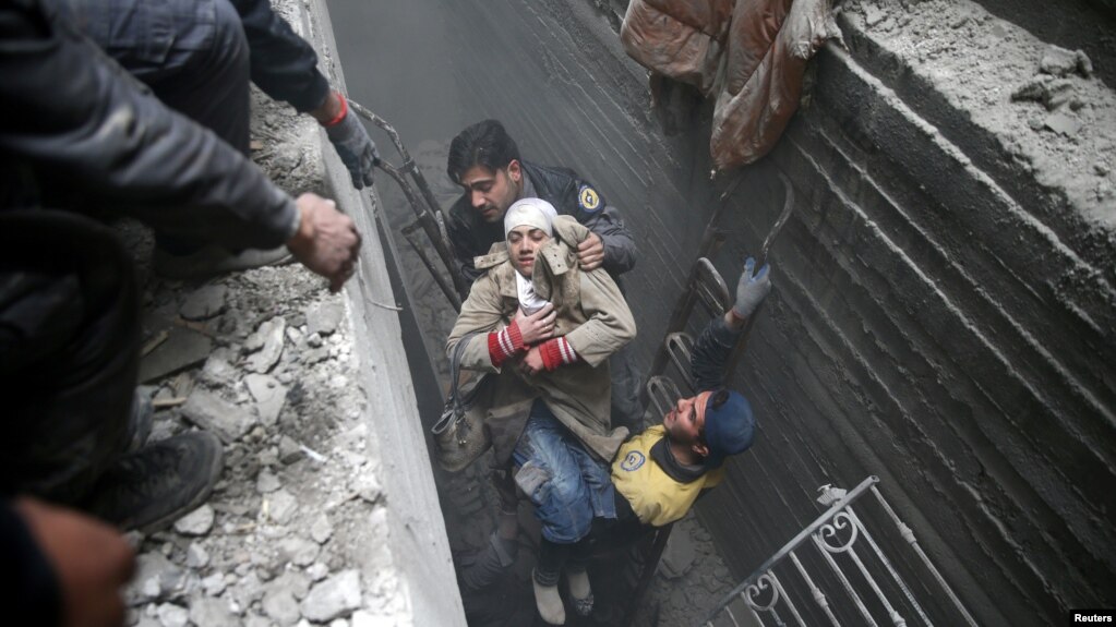 Miembros de la defensa civil siria ayudan a una mujer en un refugio en el pueblo de Douma, en el suburbio de Guta oriental.