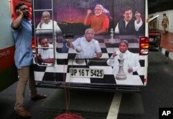 A journalist talks on his mobile phone next to an outdoor broadcasting vehicle plastered with portraits of Indian political leaders, in Bangalore, India, May 15, 2018.