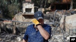 Roger Kelton, 67, wipes his tears while searching through the remains of his mother-in-law's home burned down by the Woolsey Fire, Nov. 13, 2018, in Agoura Hills, Calif. 