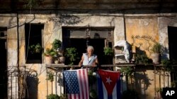 FILE - Javier Yanez stands on his balcony in Old Havana, where he hung U.S. and Cuban flags after learning that the two nations would begin restoring diplomatic ties, Dec. 19, 2014.