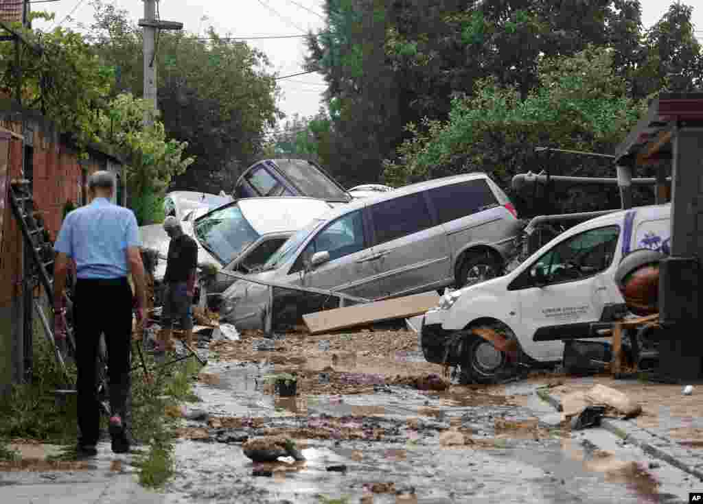 People walk through a street where cars have piled due to overnight flooding, after storms in the village of Stajkovci, just east of Skopje, Macedonia.