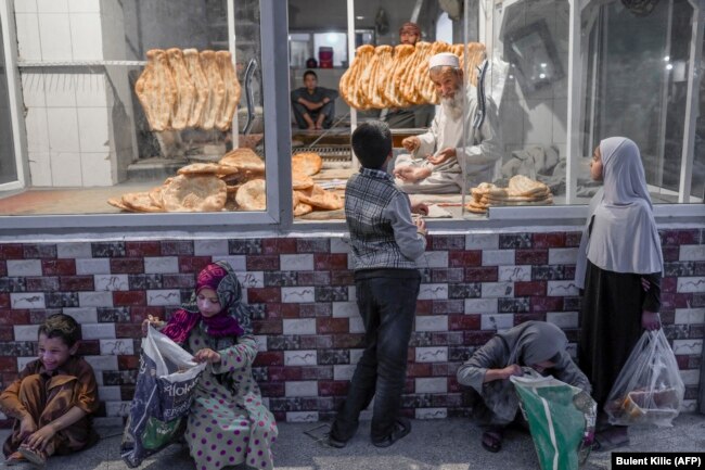 Seorang anak (tengah) menunggu giliran untuk menerima roti gratis di depan sebuah toko di Kabul, Afghanistan, 14 September 2021. (Foto: AFP/Bulent Kilic)