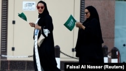 FILE - Saudi women hold national flags as they walk on a street during Saudi National Day in Riyadh, Saudi Arabia.