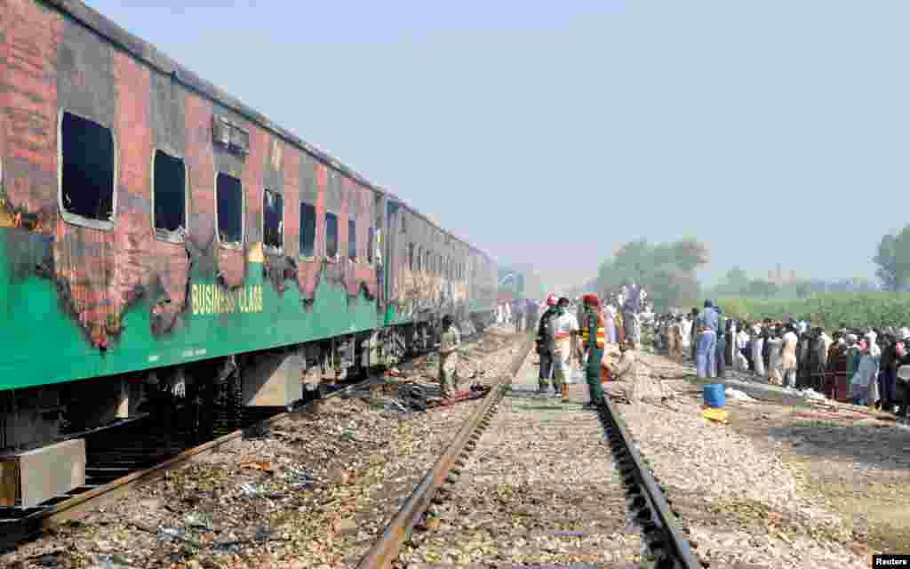 People and rescue workers gather at the scene where carriages of a passenger train destroyed by a fire near the town of Rahim Yar Khan, Pakistan.