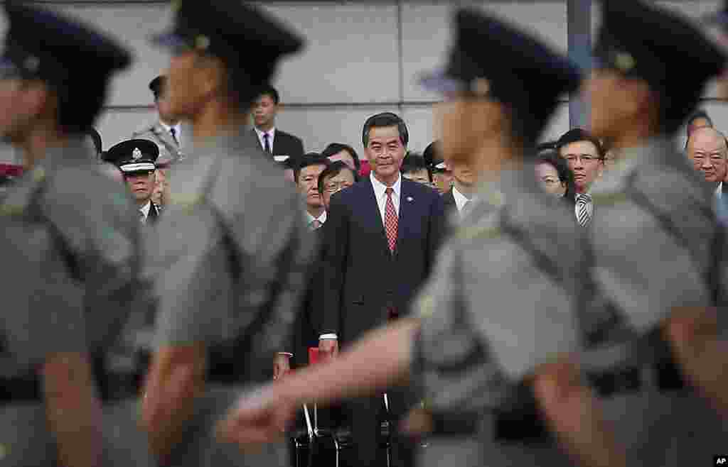 香港特区行政长官梁振英(中)观看国旗升旗仪式。军人步行。警察路障后的示威者高呼特首下台。