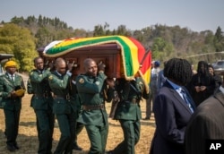 The casket of former president Robert Mugabe is carried into an air force helicopter for transport to a stadium where it will lie in state, as his widow Grace Mugabe wears a black veil, far right in background.