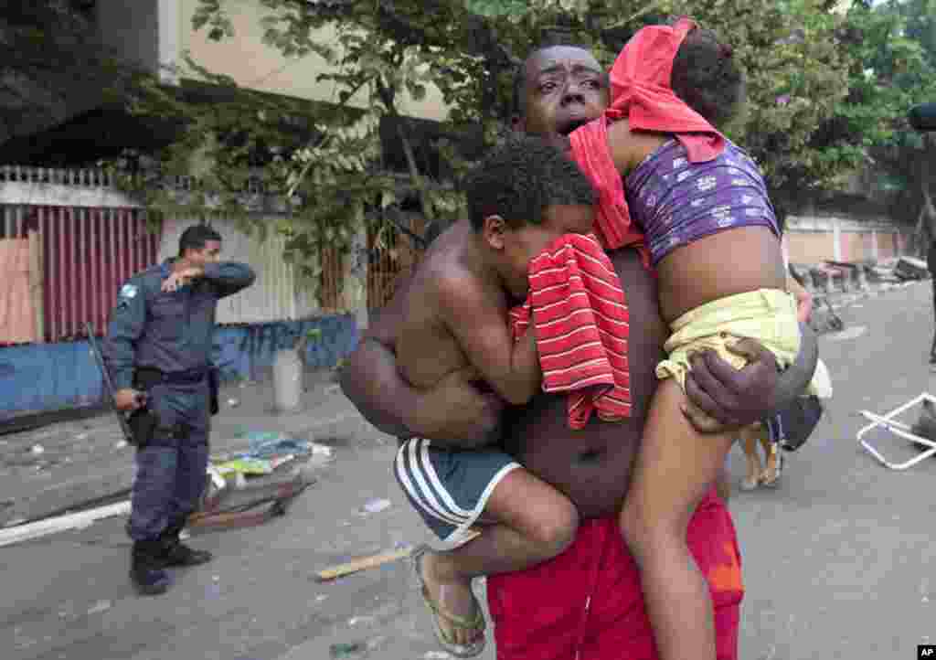 A man runs while he carries two children during an eviction in Rio de Janeiro, Brazil. Squatters in Rio de Janeiro are clashing with police after a Brazilian court ordered that 5,000 people be evicted from abandoned buildings of a telecommunications company.